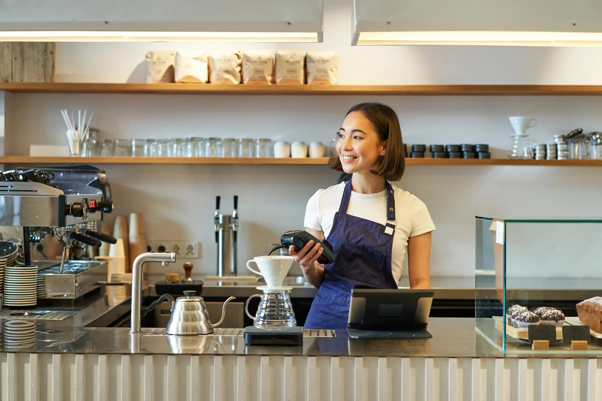 Kafede kahve demleme tezgâhının yanında gülümseyen barista