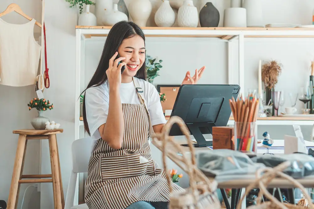 Tezgâhta tabletiyle çalışırken telefonda misafirle konuşan işletme sahibi